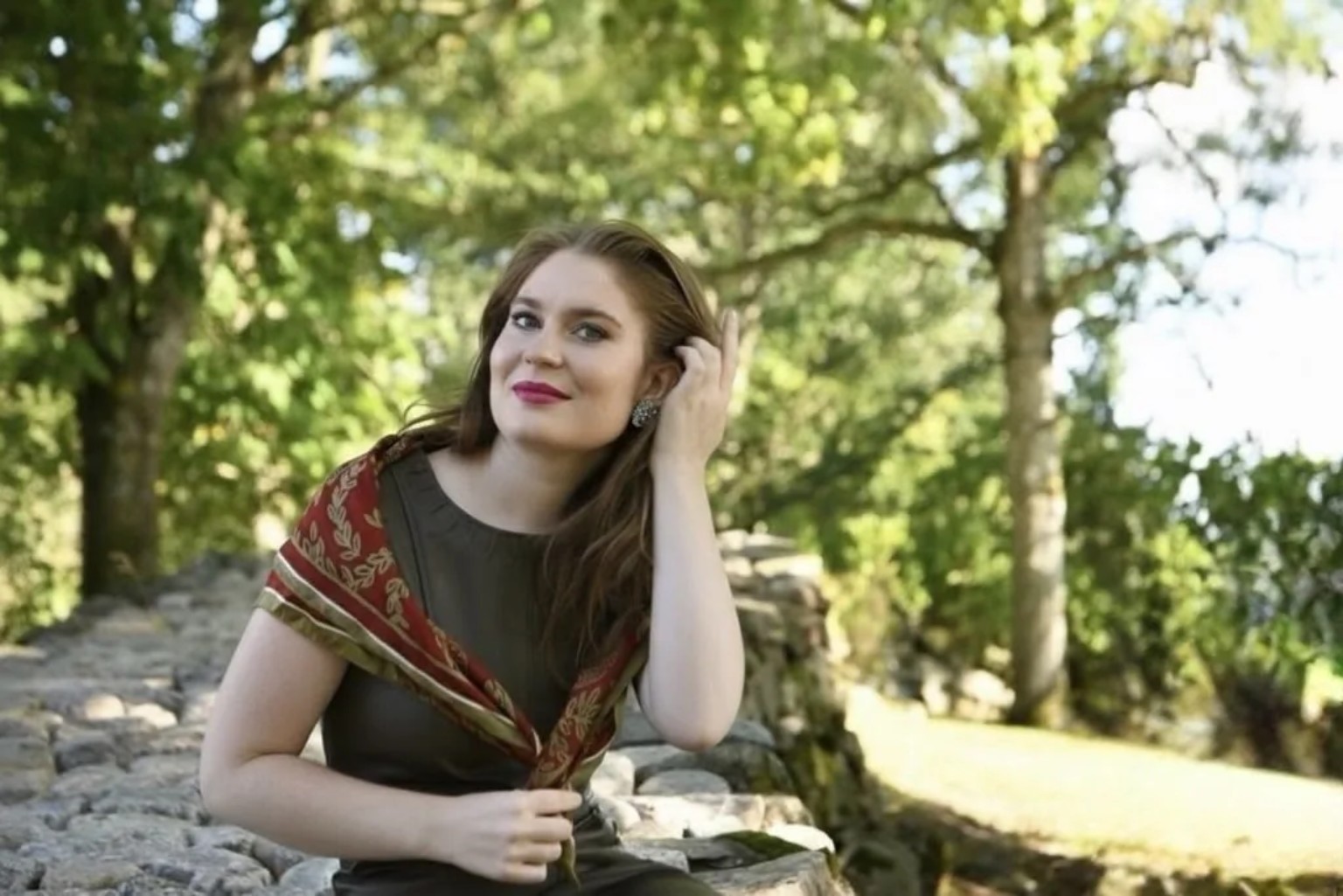 Karolina seated on a stone wall under trees in Småland
